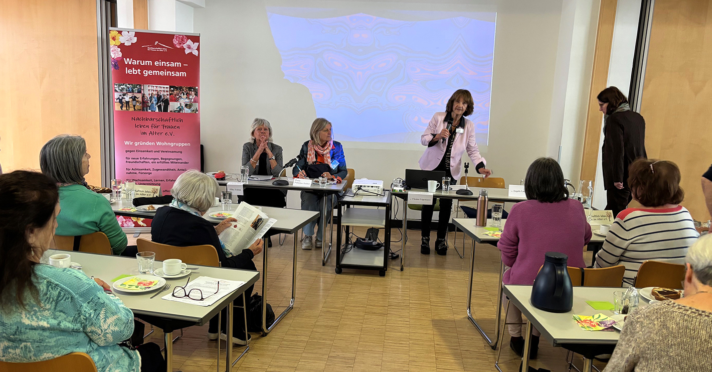 Blick auf den Vorstandstisch, links ein pinkfarbenes Rollup mit Info zum Verein.