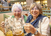 2 Frauen im Dirndl stossen am Biertisch mit einer Maß an