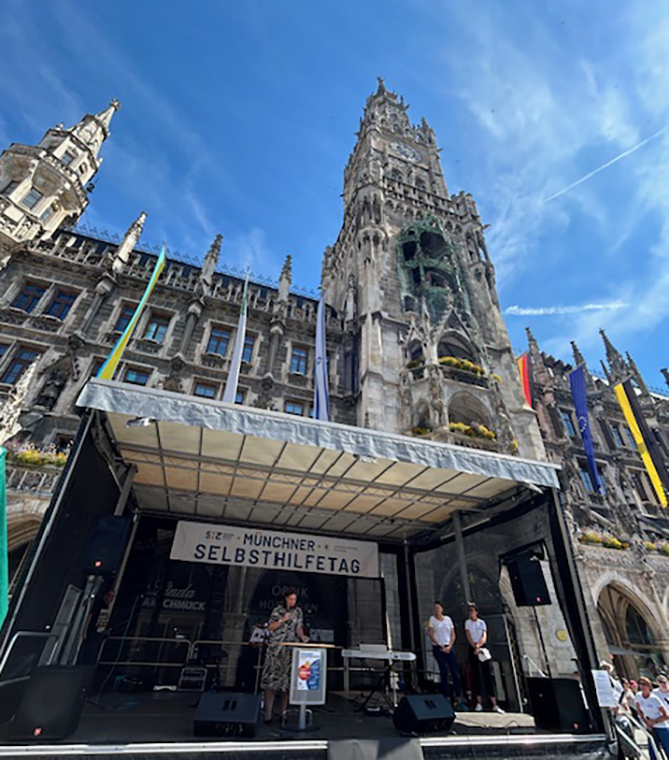 Die 3. Bürgermeisterin spricht auf der Bühne. Im Hintergrund das Rathaus vor dem strahlendblauem Himmel