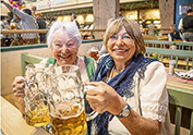 2 Frauen im Dirndl stossen am Biertisch mit einer Maß an