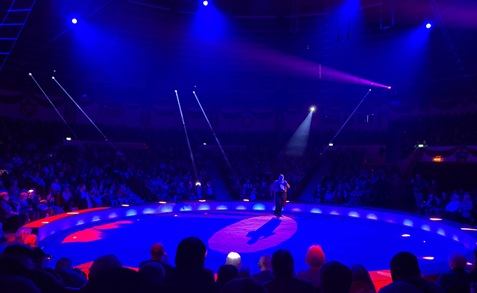 Der Zirkusdirektor im Circus Kronesteht in der lilablau leuchtenden Manege