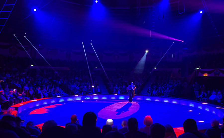 Der Zirkusdirektor im Circus Krone steht in der lilablau leuchtenden Manege