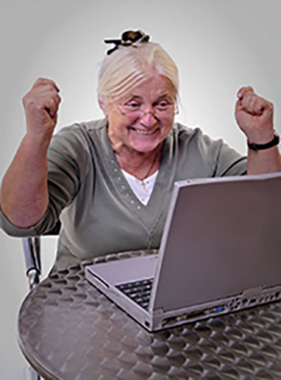 Ältere Frau am Computer freut sich über gelungenes Arbeiten damit