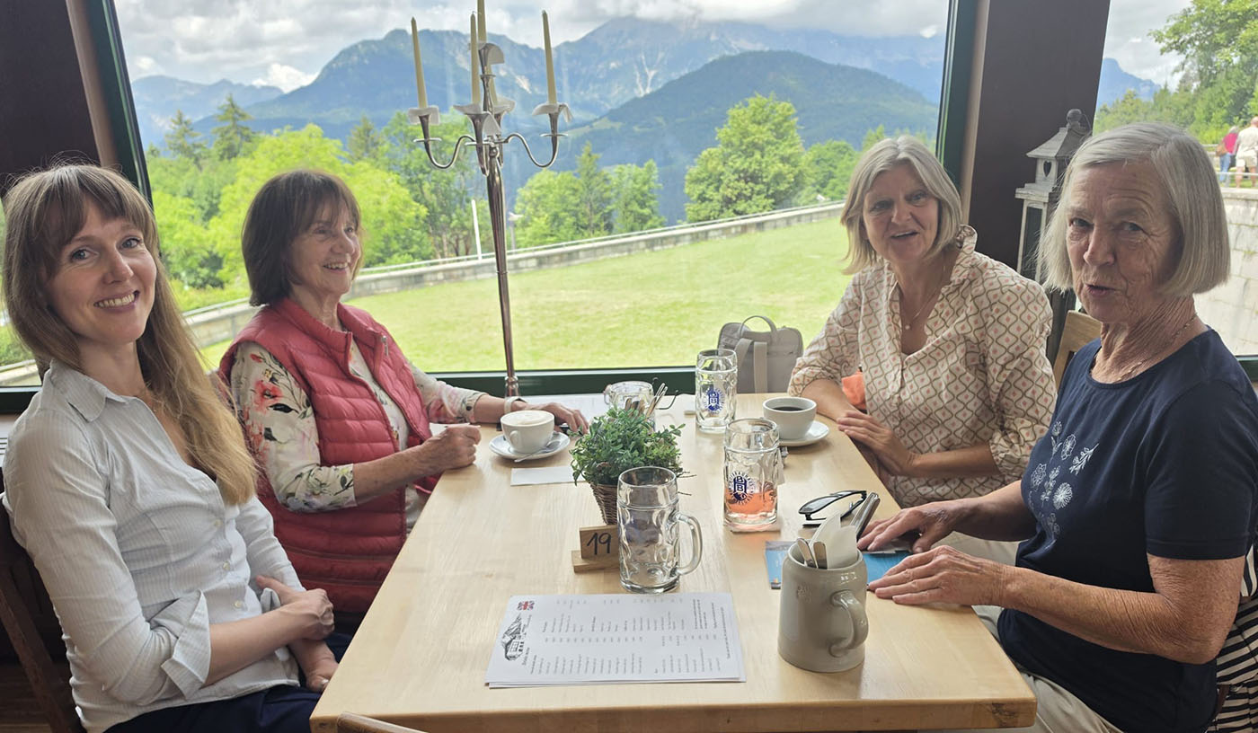 4 Frauen am Tisch beim Kaffee mit Blick auf die Berge durch das Fenster