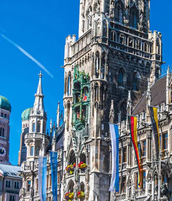 Das Münchner Rathaus von schräg vorne, im Hintergrund die Frauentürme vor strahlend blauem Himmel
